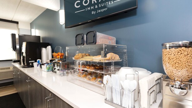 A hotel breakfast buffet with various food items, a TV screen above, and a coffee machine. - Coratel Inn & Suites by Jasper Mankato (Mankato)
