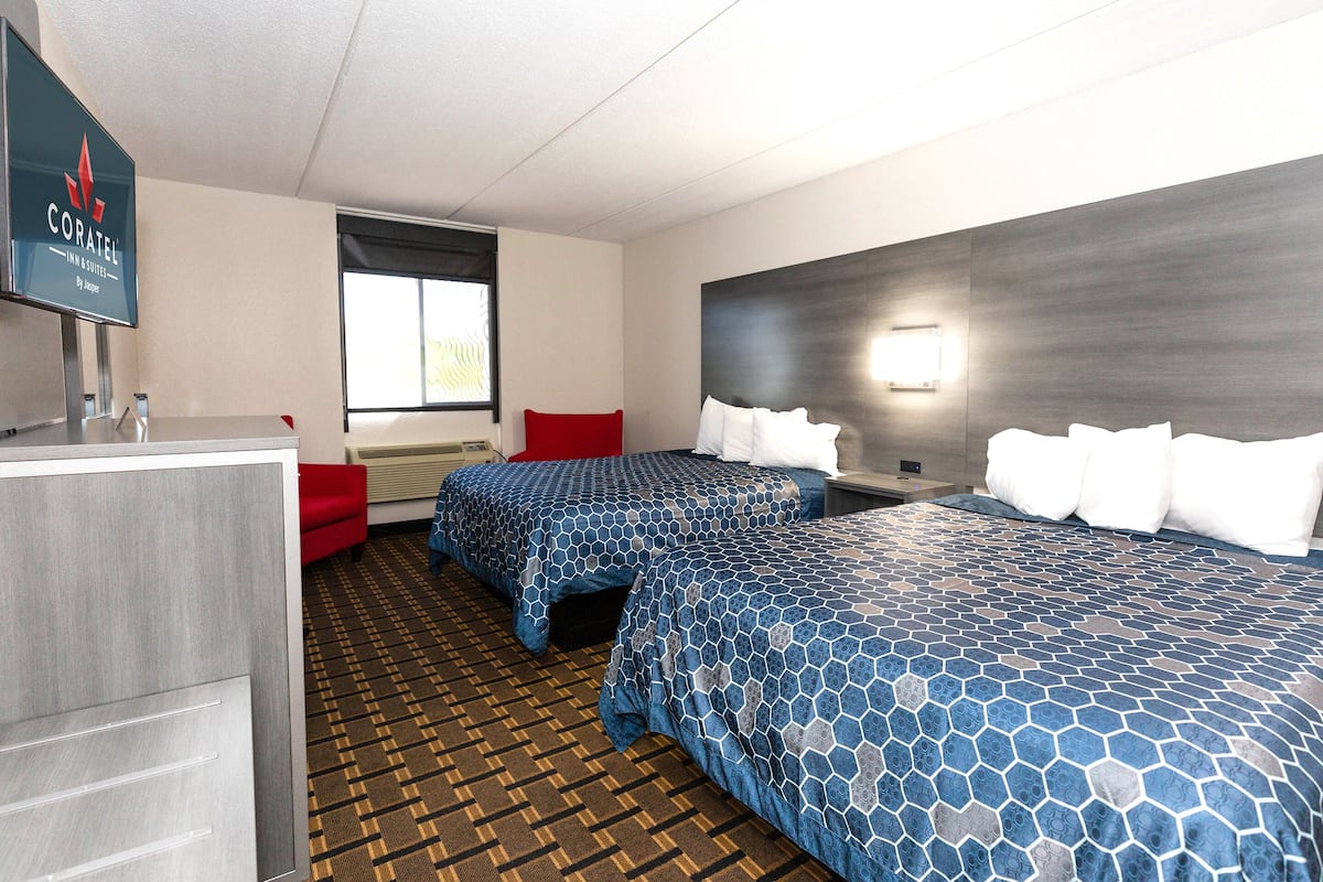 Ein Hotelzimmer mit zwei Betten, einem Schreibtisch, einem Fernseher und einem Fenster.