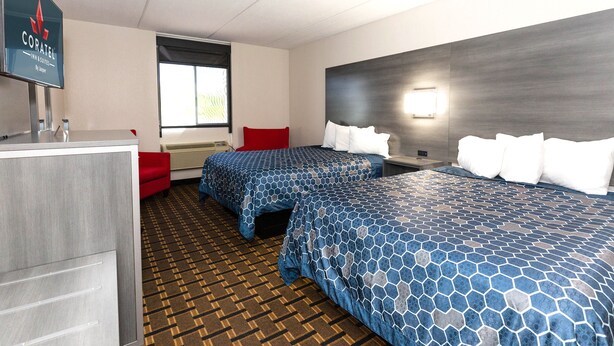 A hotel room with two beds, a desk, a TV, and a window.