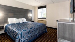 A hotel room with a bed, a nightstand, a TV, and a window.