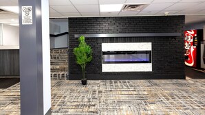A modern lobby with a black brick wall, a large flat-screen TV, a potted plant, and a Coca-Cola vending machine. - Coratel Inn & Suites by Jasper Mankato (Mankato)