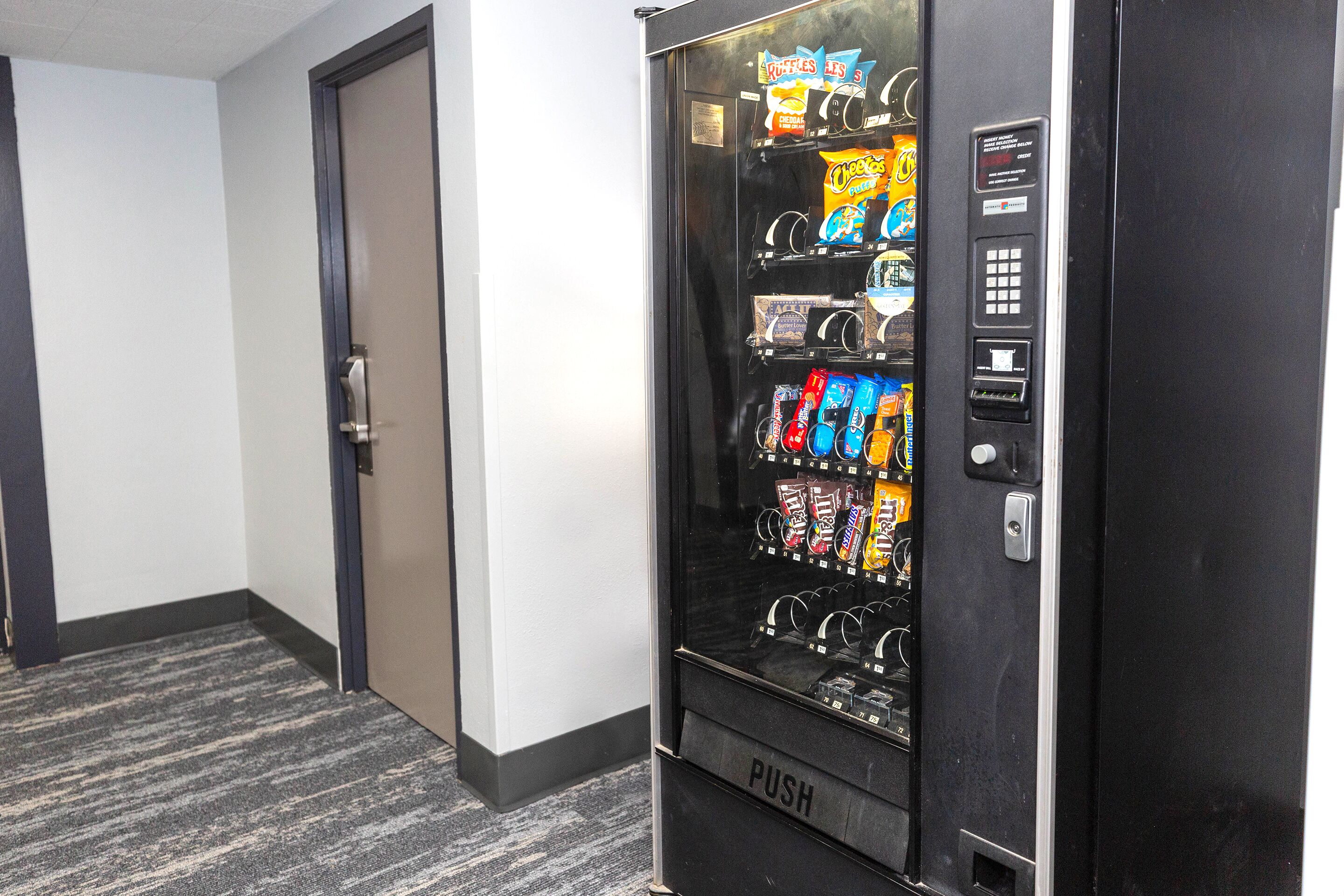 A vending machine with snacks and drinks in a hallway.