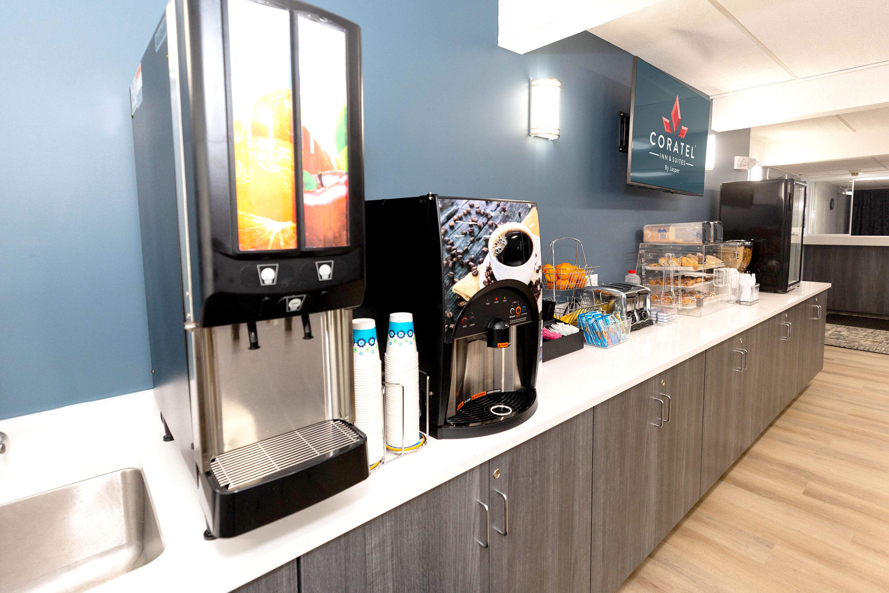 A hotel bar area with a coffee machine, a TV screen, and a Coratel sign.