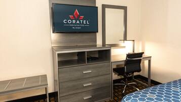 A hotel room with a bed, a desk, a chair, a TV mounted on the wall, and a dresser with drawers.