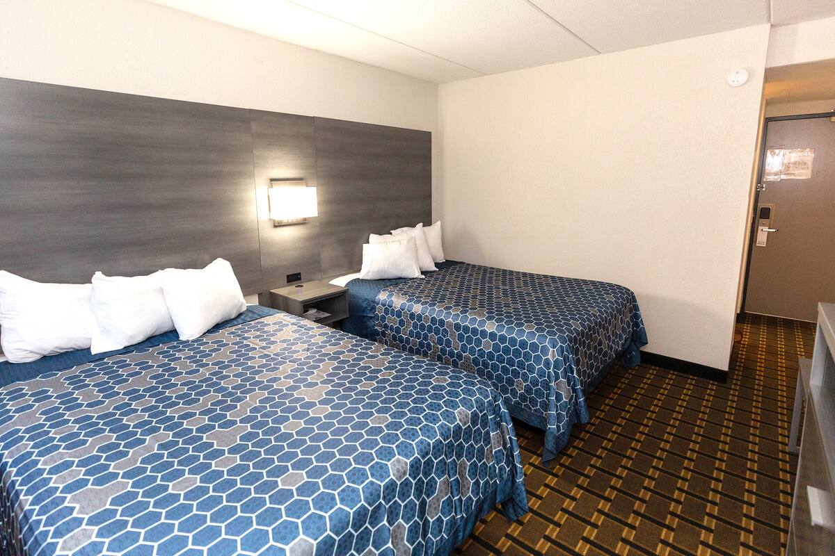 Ein Hotelzimmer mit zwei Betten, einem Nachttisch, einer Wandleuchte und einer Tür.