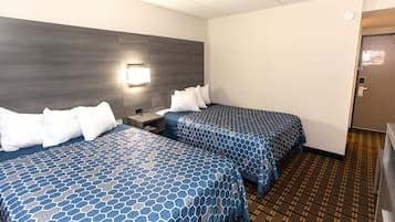 A hotel room with two beds, a nightstand, a wall-mounted light, and a door.