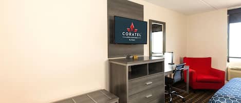 A hotel room with a bed, a desk, a chair, a dresser, and a television mounted on the wall.