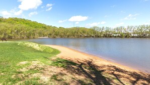 A lakeside park with a bench, grassy areas, and a clear sky.