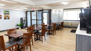 A dining area with wooden tables and chairs, a vending machine, and a refrigerator.