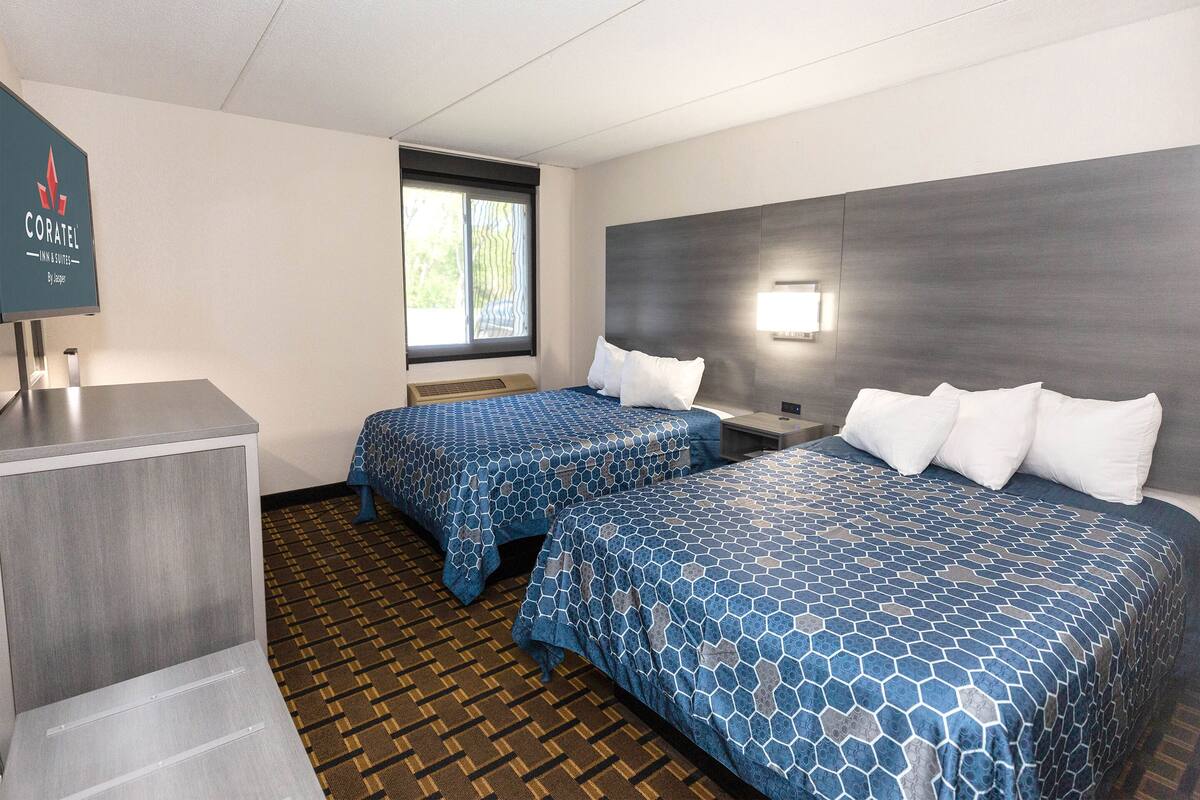 Ein Hotelzimmer mit zwei Betten, einem Schreibtisch, einem Fenster mit Jalousien und einer Wandleuchte.