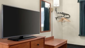 Habitación de hotel con televisión de pantalla plana sobre un escritorio de madera, un espejo, una lámpara de pared y un perchero.