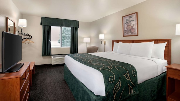 Una habitación de hotel con una cama, televisión, escritorio, silla y ventana con cortinas.