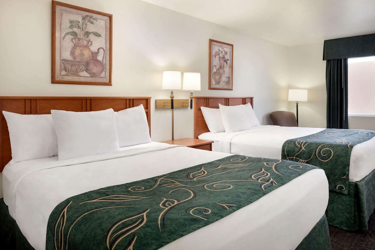 Een hotelkamer met twee bedden, elk met witte lakens en groene dekens. Er zijn twee wandlampen en kunstwerken in lijsten boven de bedden.