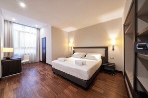 A hotel room with a large bed, bedside lamps, a desk with a lamp, a chair, and a wardrobe. - Hotel Leonardo Da Vinci (Florence)