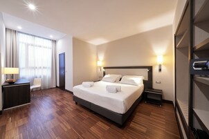 Una camera d'albergo con un letto grande, abat-jour sui comodini, una scrivania con lampada, una sedia e un armadio.
