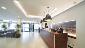 A modern reception desk with two staff members, a seating area with sofas, and a cityscape view.