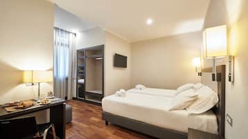 Quarto de hotel com cama, escrivaninha, cadeira e televisão.