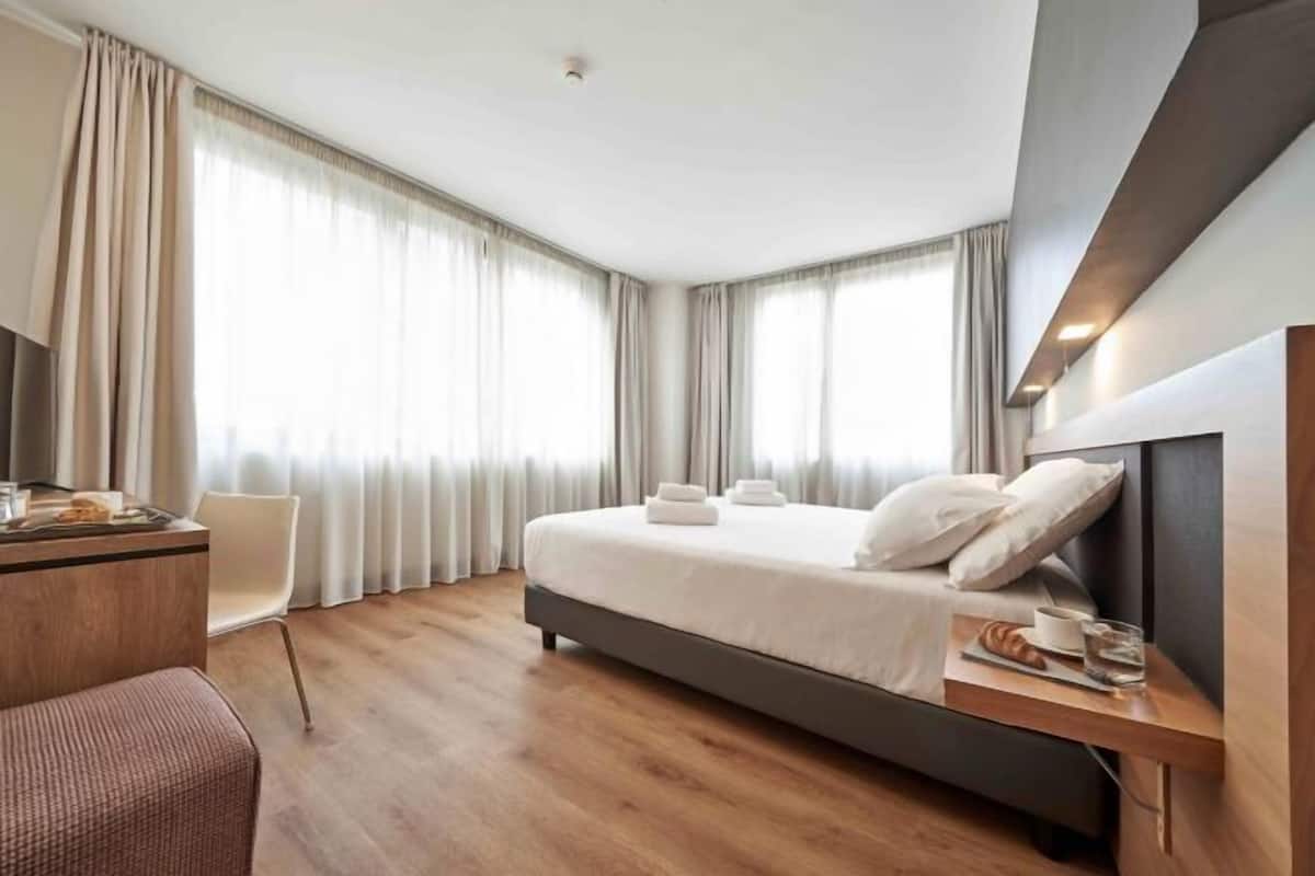 A modern hotel room with a bed, a desk, and a chair.