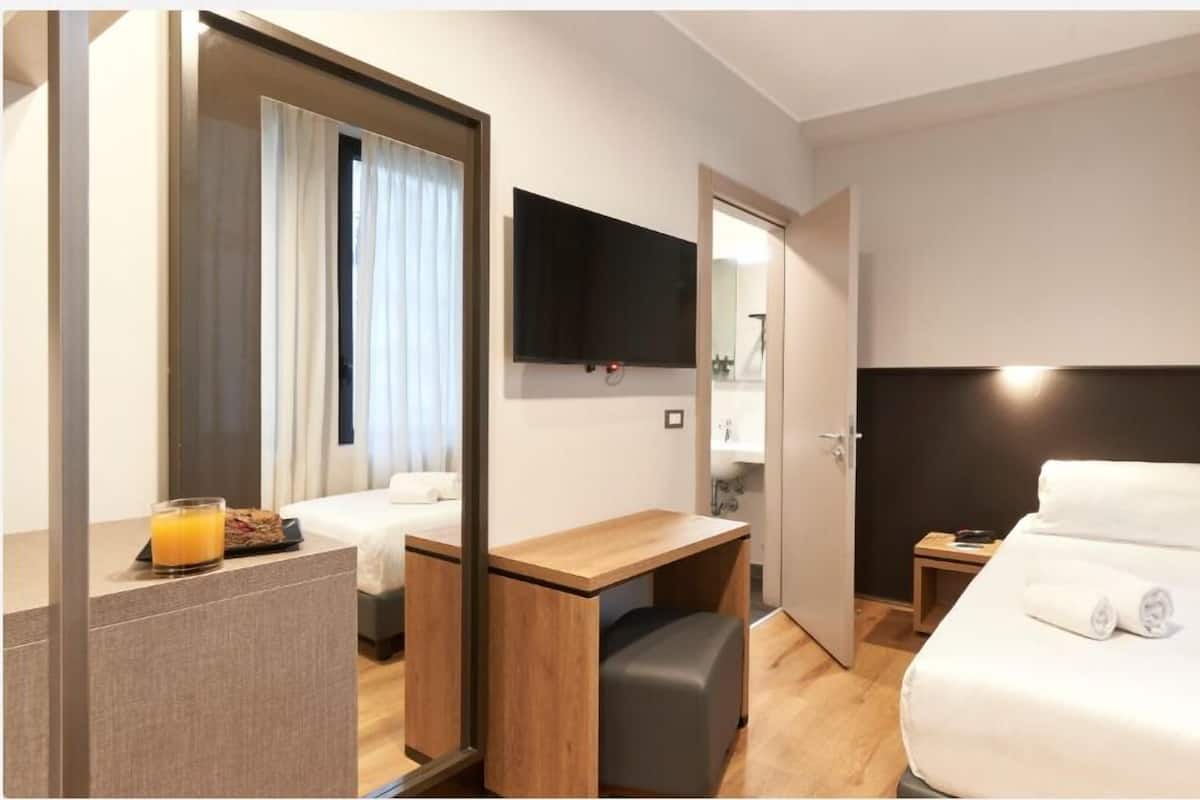 A hotel room with a bed, a desk, a chair, a TV, and a bathroom visible through an open door.