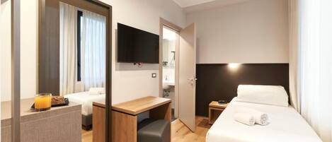 Habitación de hotel con cama, escritorio, silla, televisor y baño visible a través de una puerta abierta.