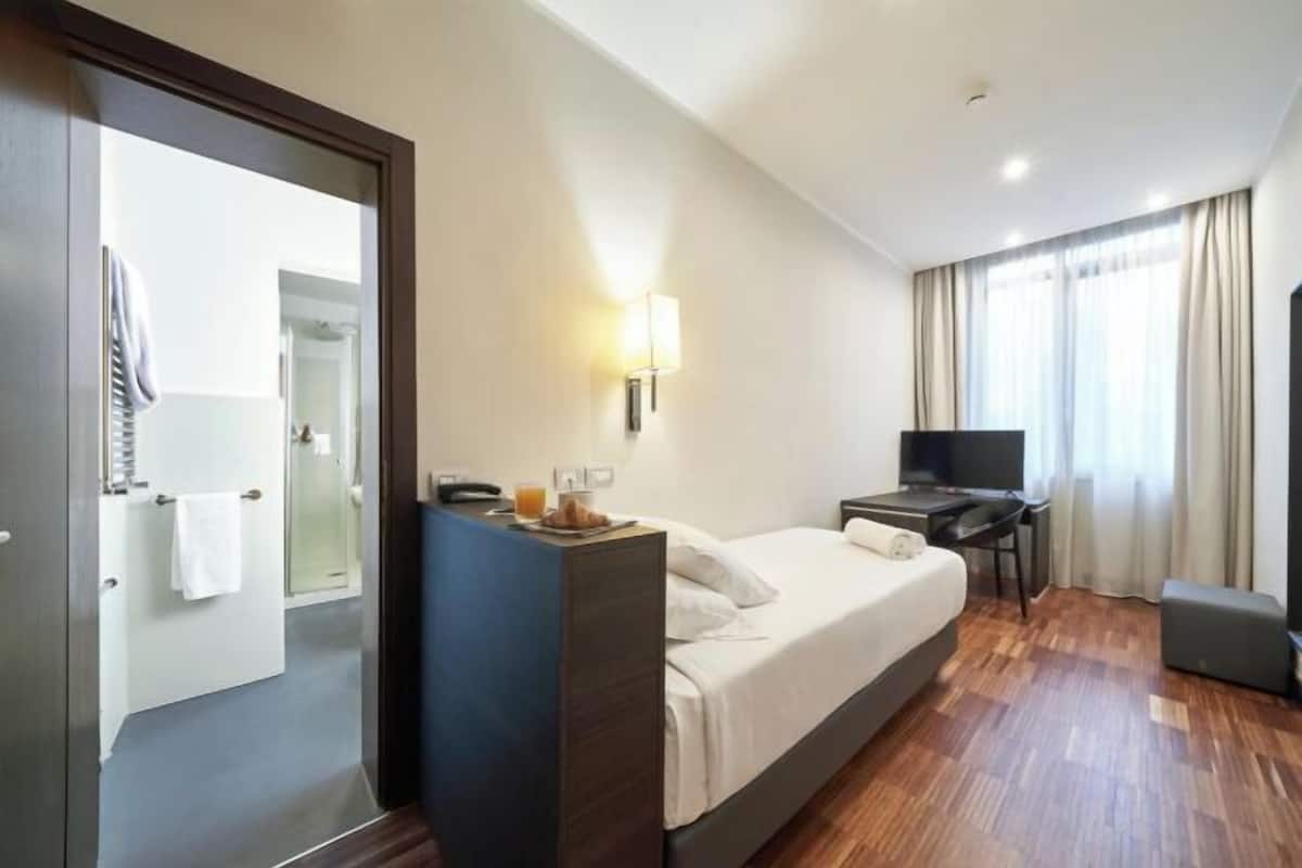 A hotel room with a bed, desk, chair, and a television.