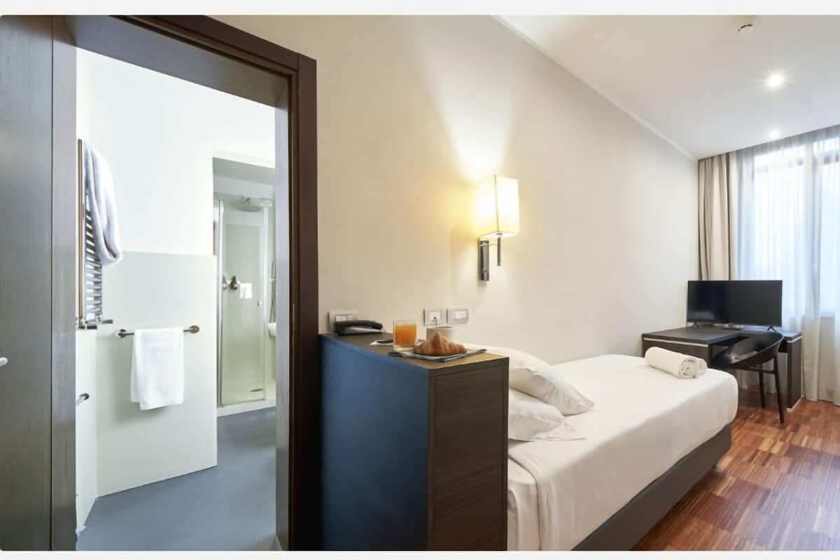 A hotel room with a bed, a desk with a TV, a chair, and a bathroom visible through an open door.