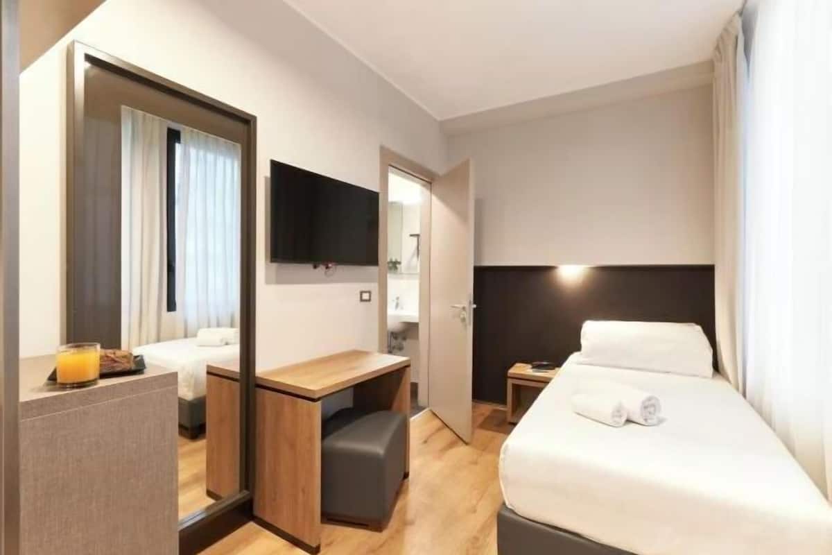 A hotel room with a bed, a desk, a chair, a TV, and a mirror.