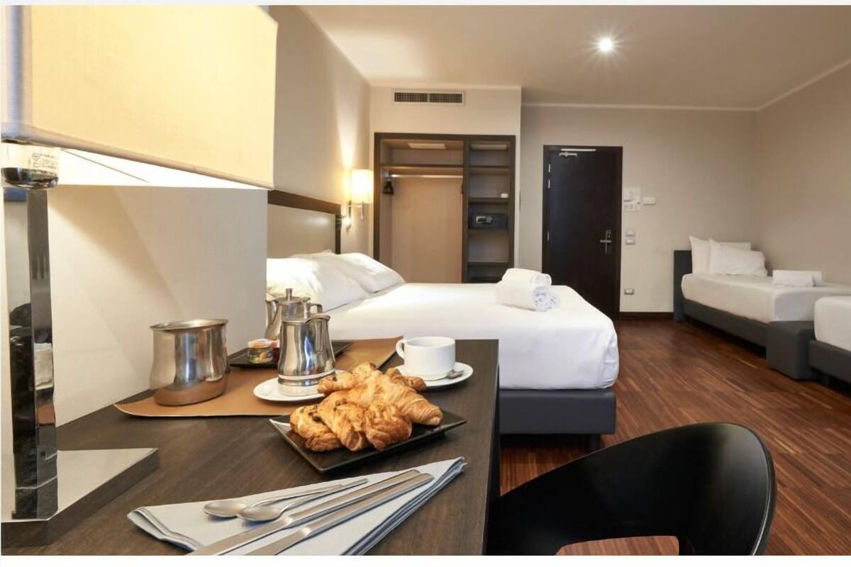 A hotel room with a bed, a desk with breakfast items, a chair, and a TV mounted on the wall.