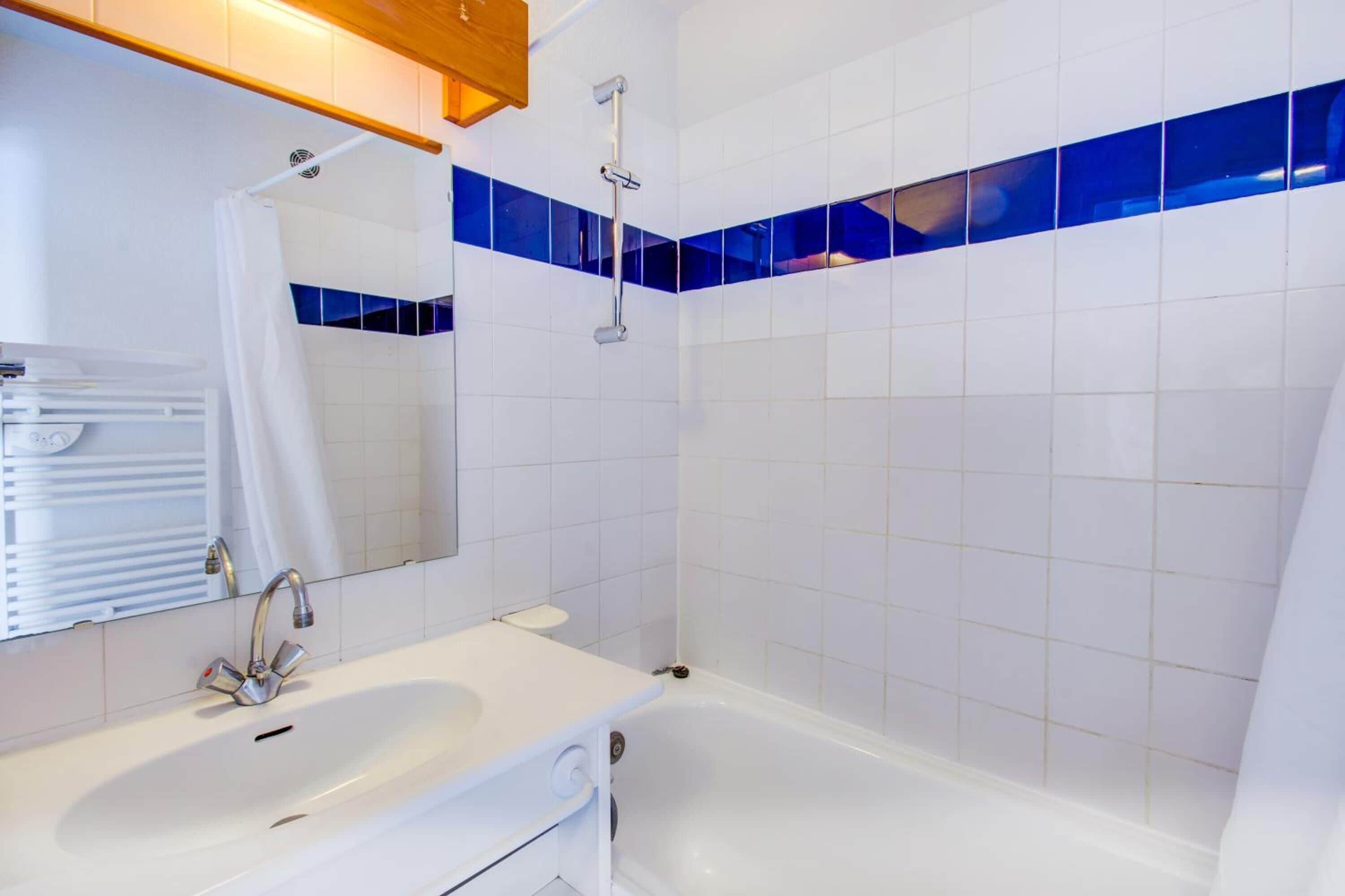 Une salle de bain avec un lavabo blanc, un miroir, une douche et des murs recouverts de carreaux bleus.