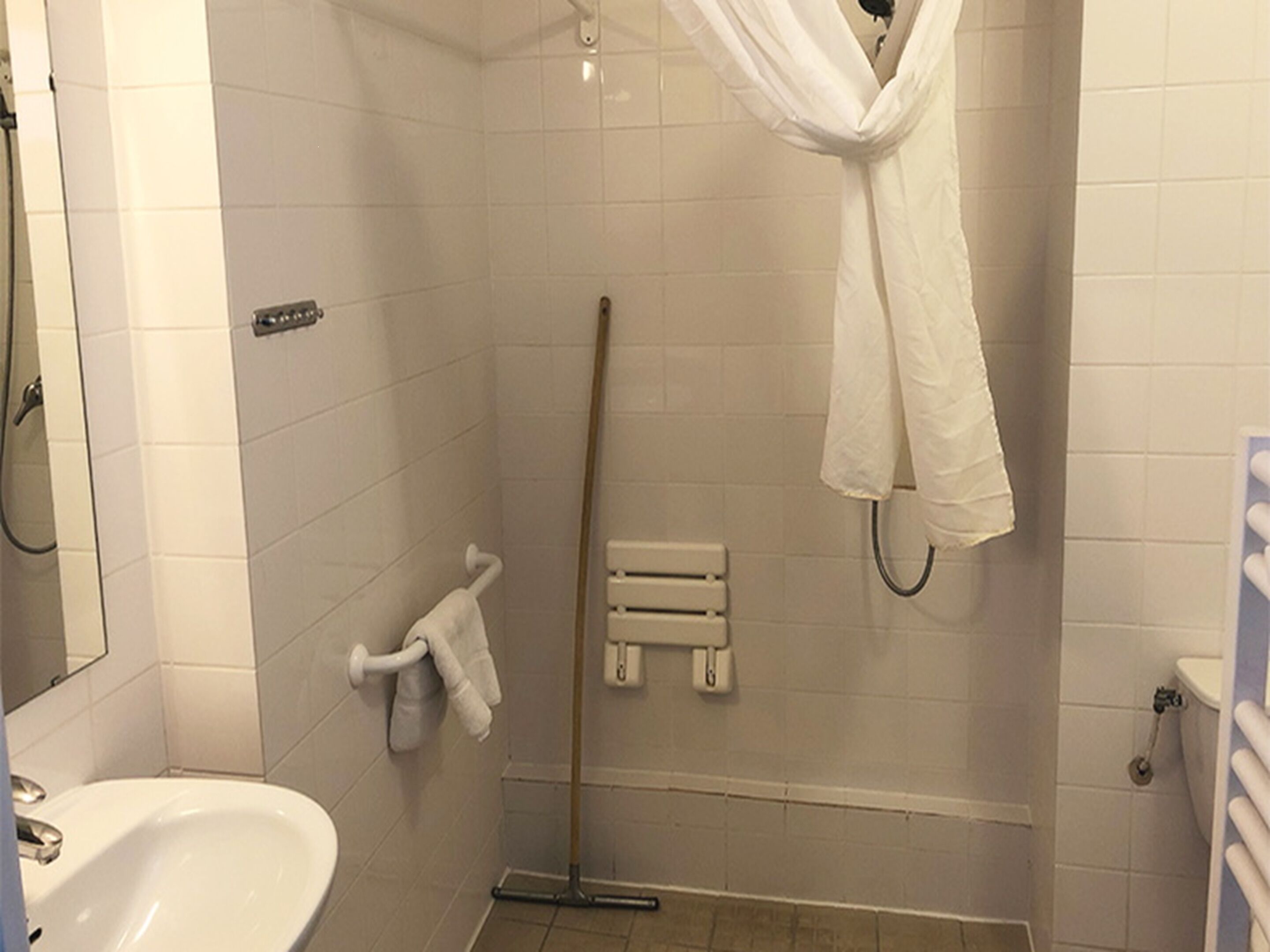 Een badkamer met een wit wastafel, een douche met een witte gordijn en een handdoekrek.