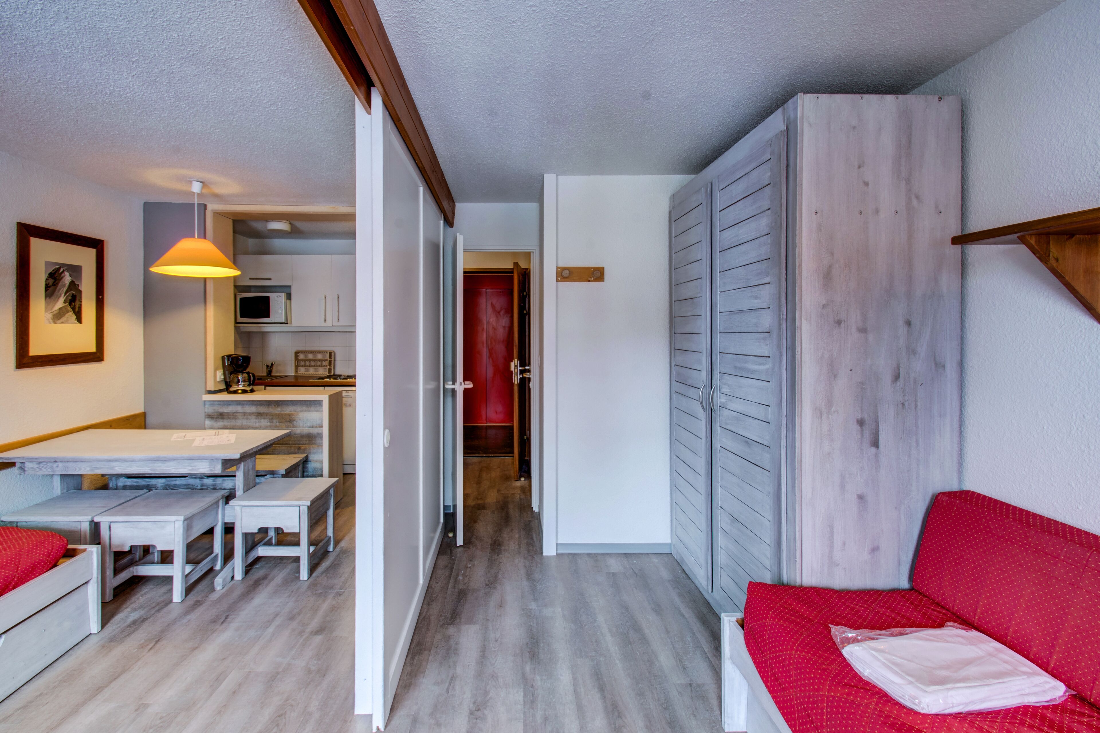 Ett kompakt bostadsutrymme med en matplats, ett litet kök och en röd soffa.