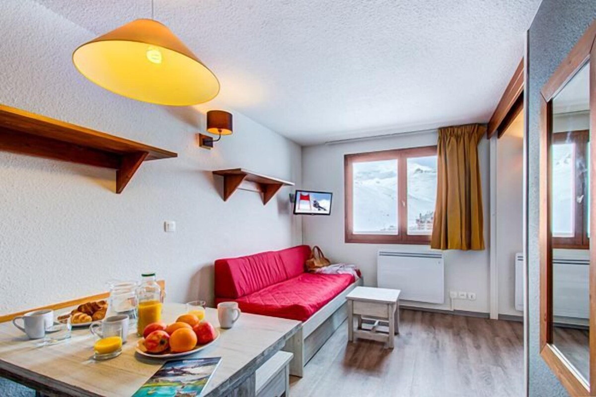 A cozy room with a red sofa, a small table with breakfast items, a TV on the wall, and a window with a view of the outdoors.