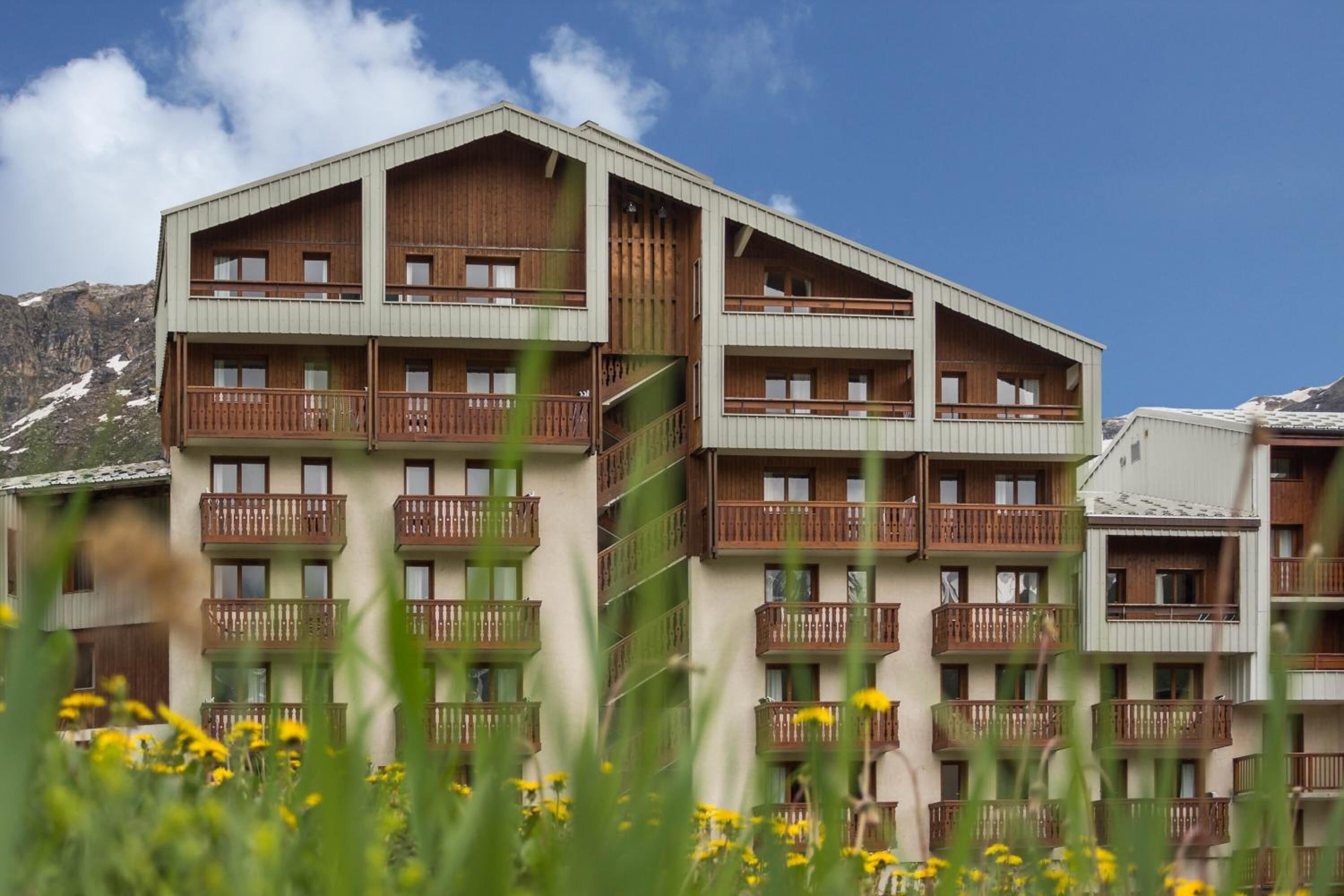 Un hotel de diversos pisos amb balcons, fons de muntanya i cel blau.
