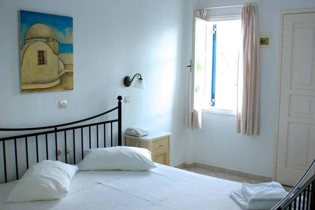 Un dormitorio con cama, mesita de noche, lámpara, un cuadro y una ventana con cortinas.