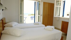 A hotel room with two beds, a wooden wardrobe, and a view of the sea through open doors. - Hotel Blue Bay Villas (Santorini)
