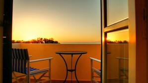 A balcony with a table and two chairs, overlooking a sunset. - Hotel Blue Bay Villas (Santorini)