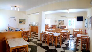 A hotel room with a checkered floor, wooden furniture, a kitchen area, and artwork on the walls. - Hotel Blue Bay Villas (Santorini)