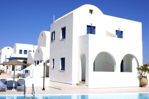 Een wit gebouw met blauwe accenten, een zwembad en ligbedden.