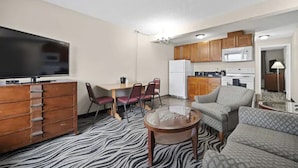 Ein kompakter Wohnbereich mit Flachbildfernseher, Essbereich mit Stühlen, einer Couch, einer Küche mit Schränken und Geräten sowie einem zebra-gemusterten Teppich.