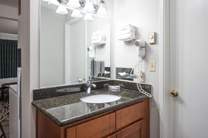 A bathroom with a granite countertop sink, a mirror, a hairdryer, and a towel rack.
