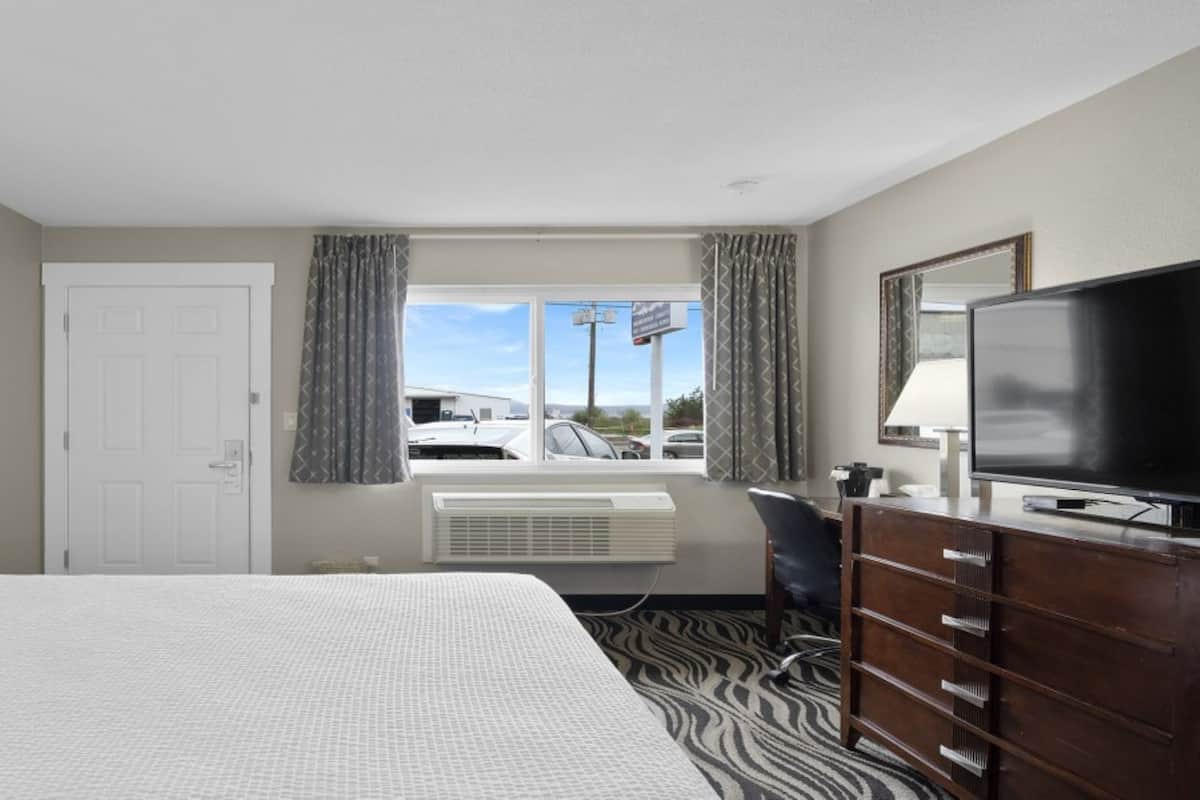 A hotel room with a large bed, a desk, a television, and a view of the parking lot.