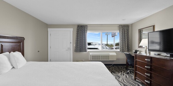 A hotel room with a large bed, a desk, a television, and a view of the parking lot.