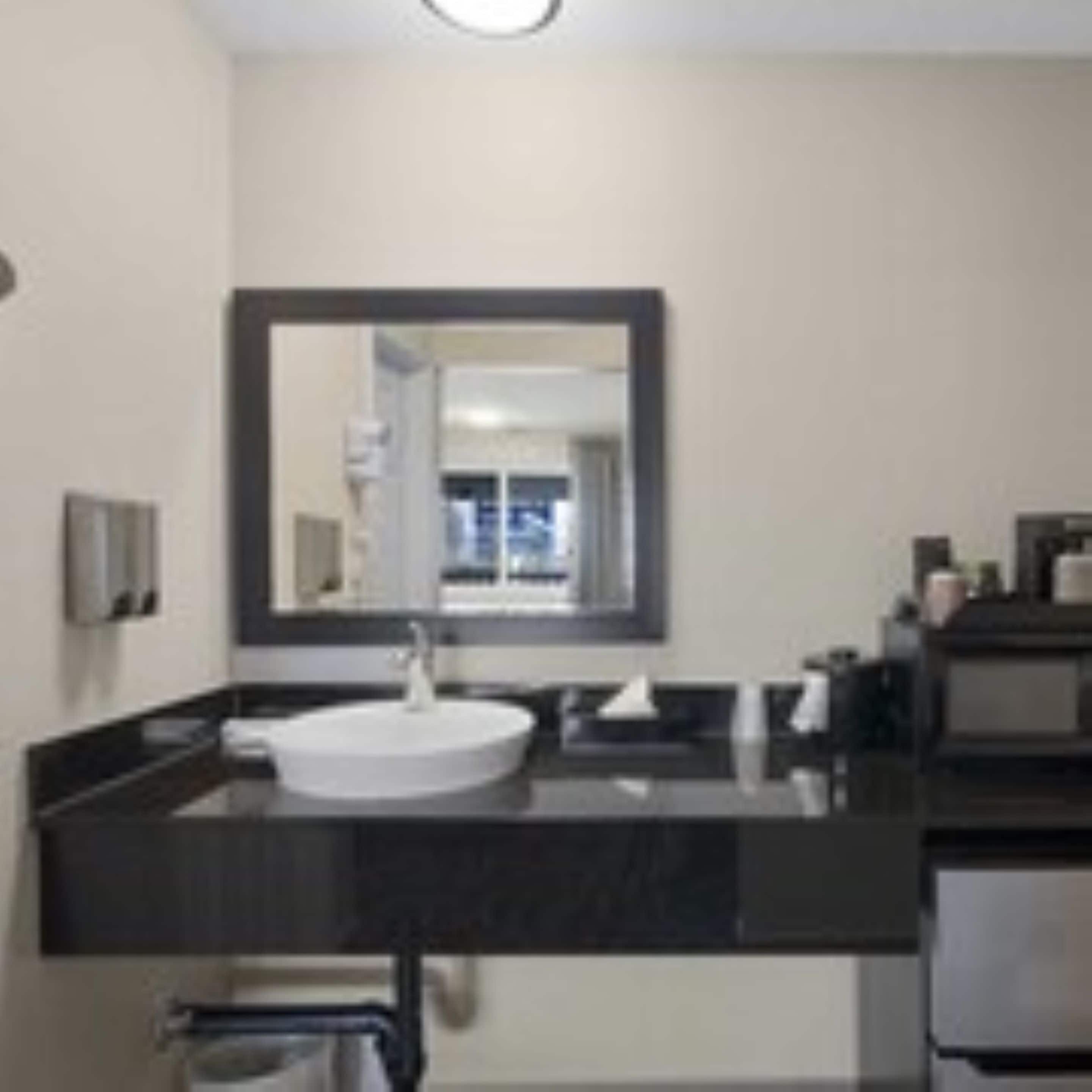 Un baño moderno con un espejo grande, un lavabo blanco y encimeras oscuras.