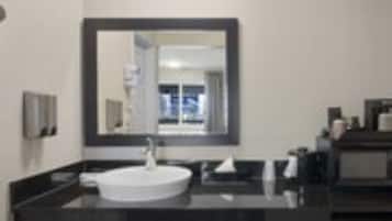 Un baño moderno con un espejo grande, un lavabo blanco y encimeras oscuras.