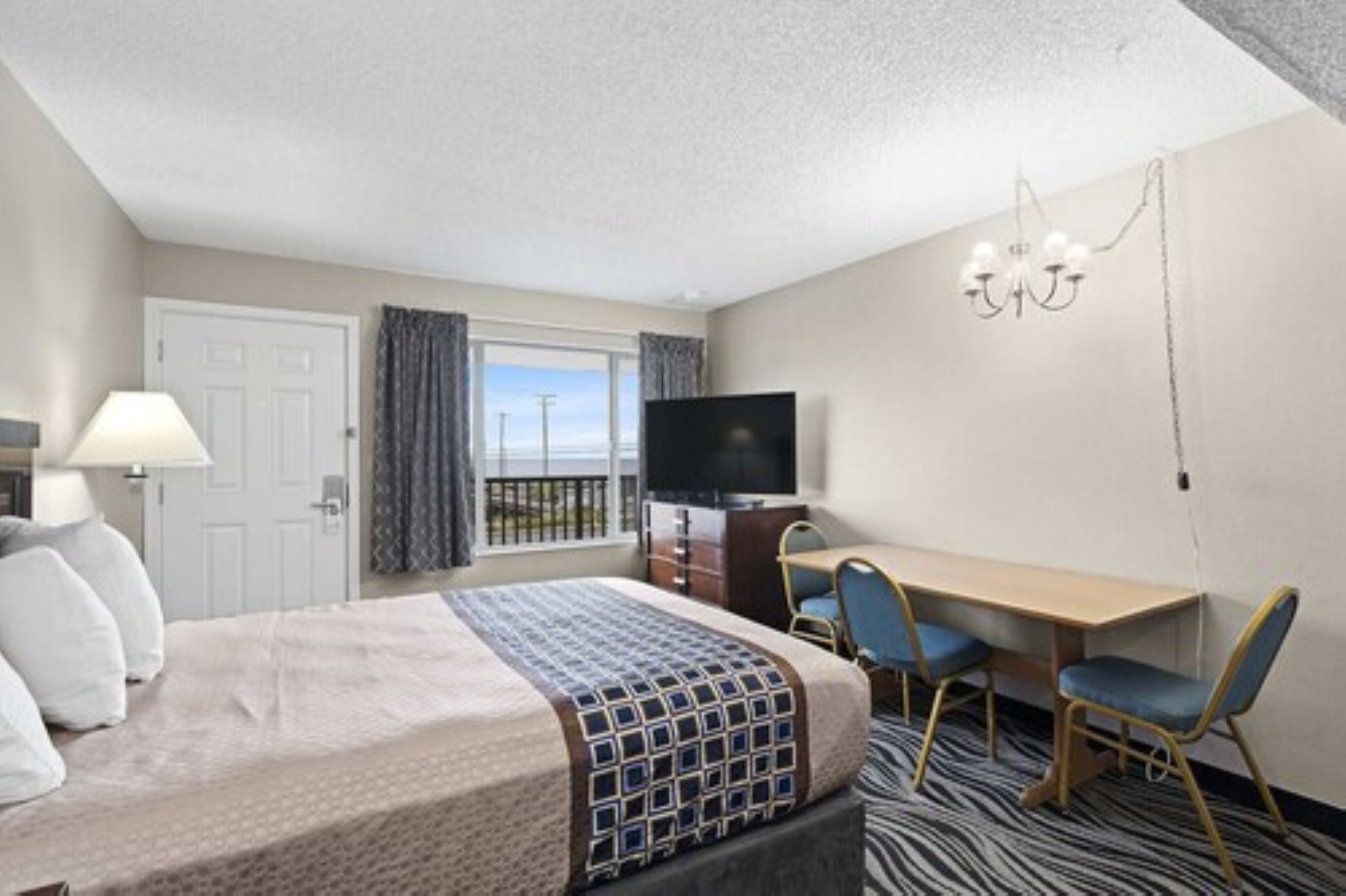 A hotel room with a bed, a desk with two chairs, a television, and a window with curtains.
