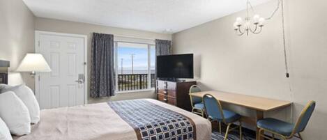 A hotel room with a bed, a desk with two chairs, a television, and a window with curtains.