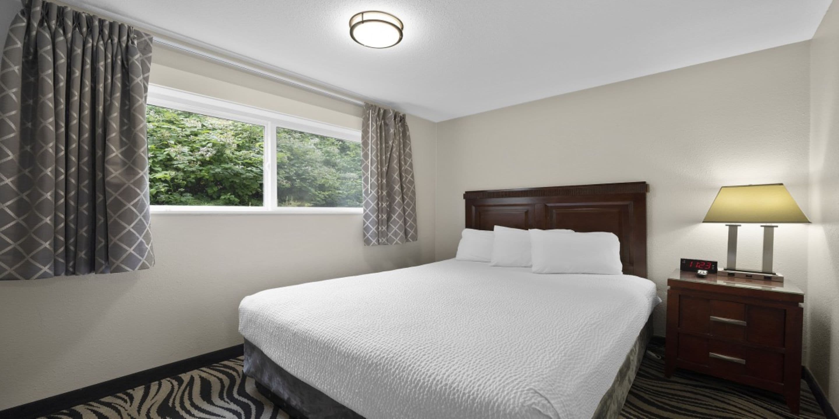 A hotel room with a large bed, a nightstand with a lamp, and a window with curtains.