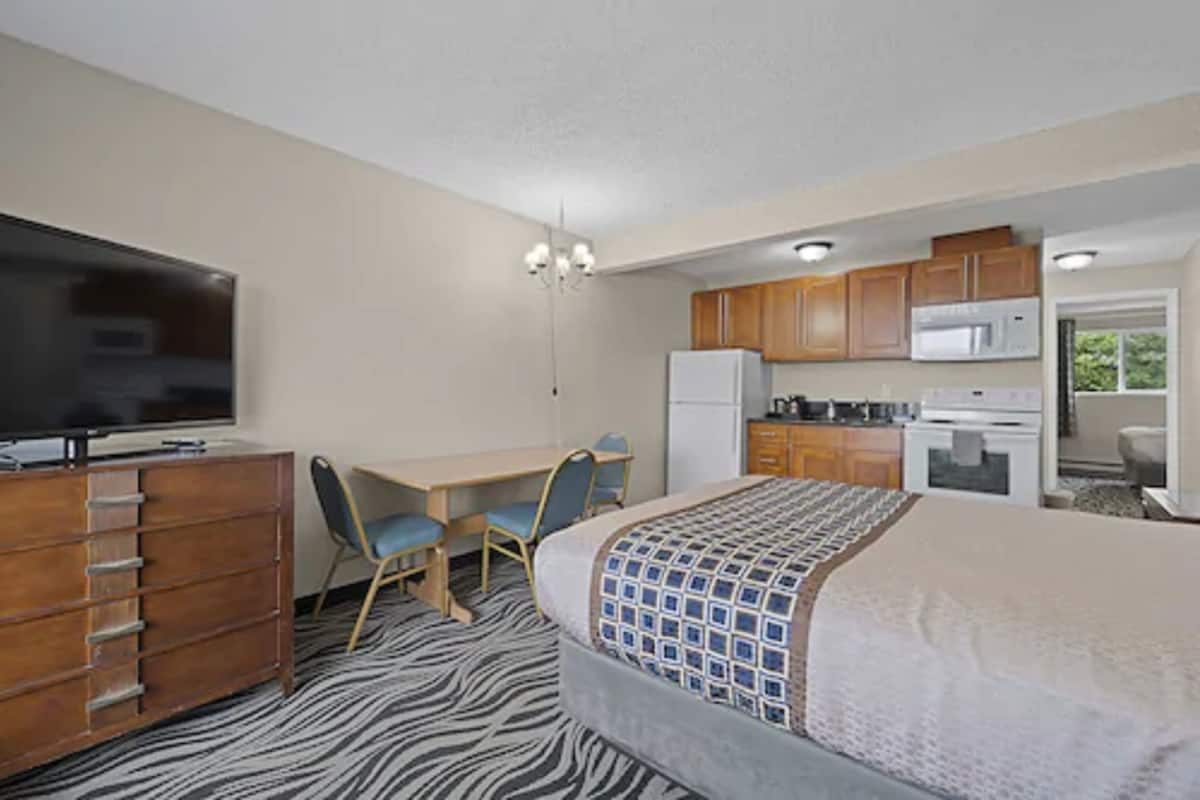 A compact hotel room with a bed, a desk, a chair, a television, a refrigerator, a microwave, and a kitchenette.