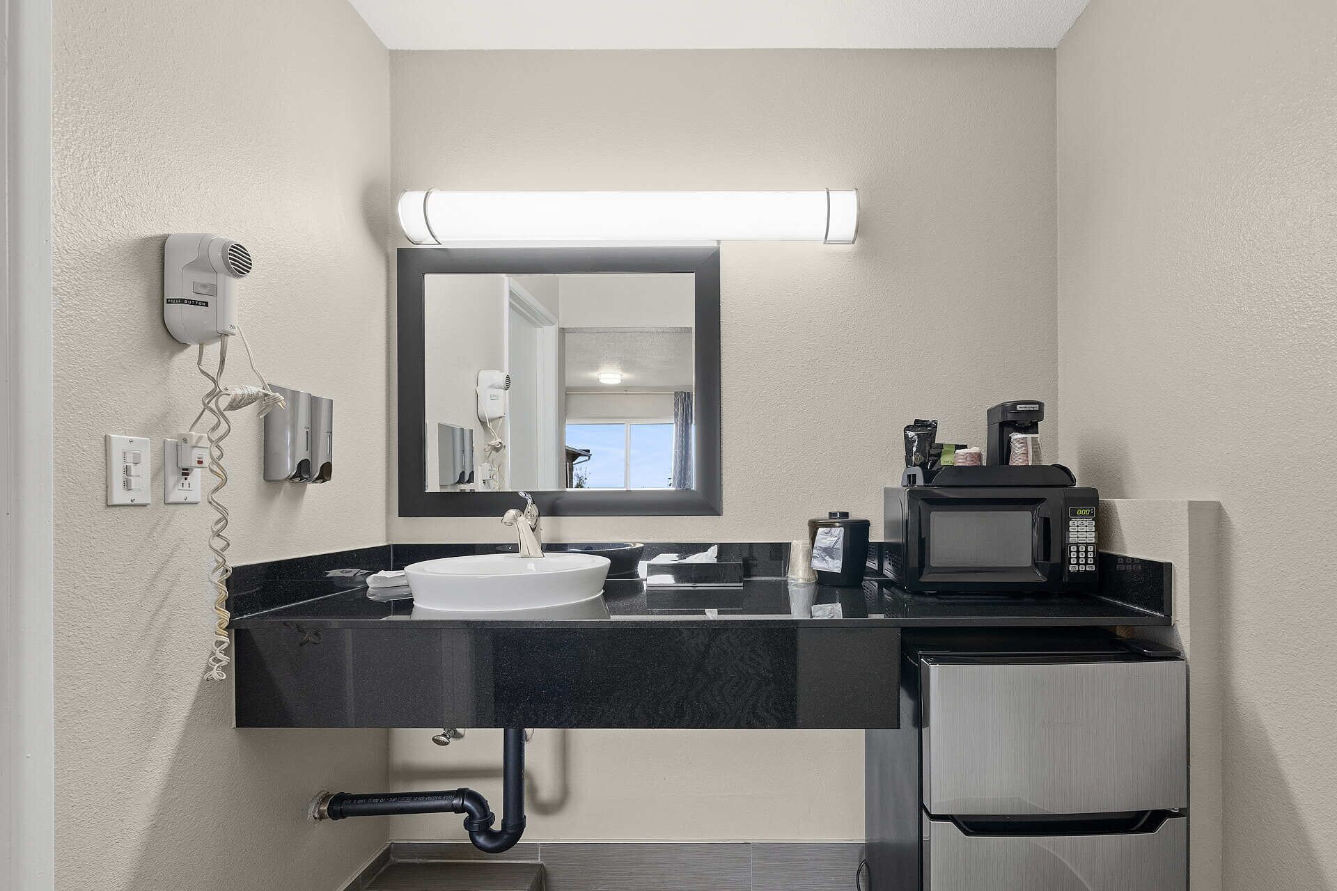 A modern bathroom with a sink, mirror, hair dryer, and coffee maker.