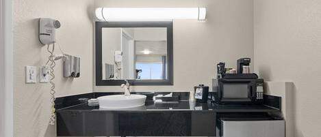 A modern bathroom with a sink, mirror, hair dryer, and coffee maker.